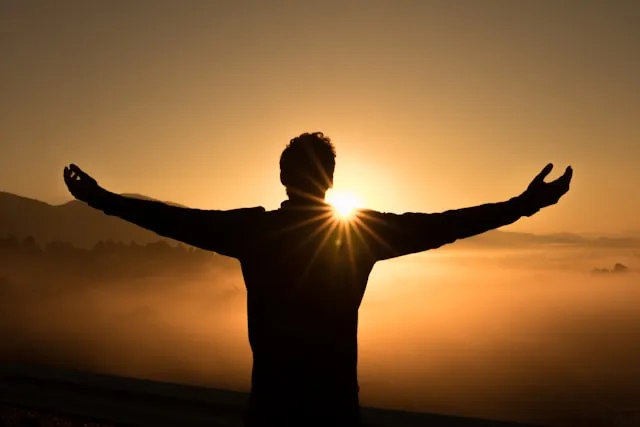 Persona con los brazos abiertos al atardecer, en libertad y satisfacción